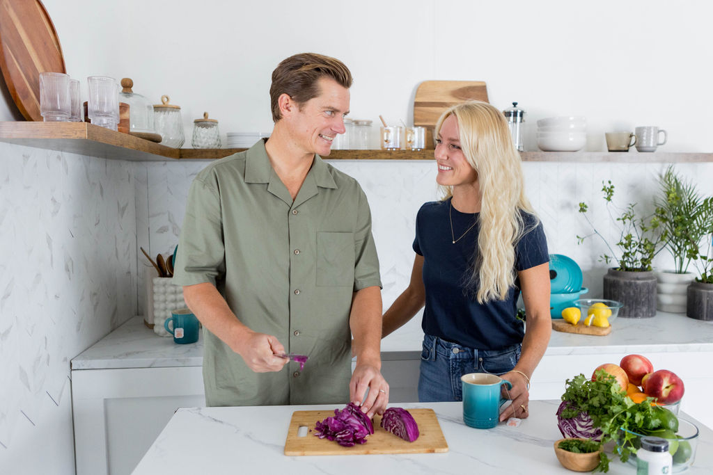 Man and woman in the kitchen cutting up a red onion while talking to each other.