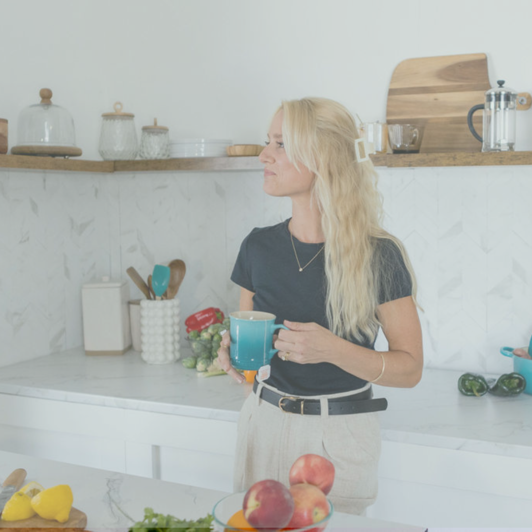 Blonde woman standing in the kitchen drinking a cup of tea.