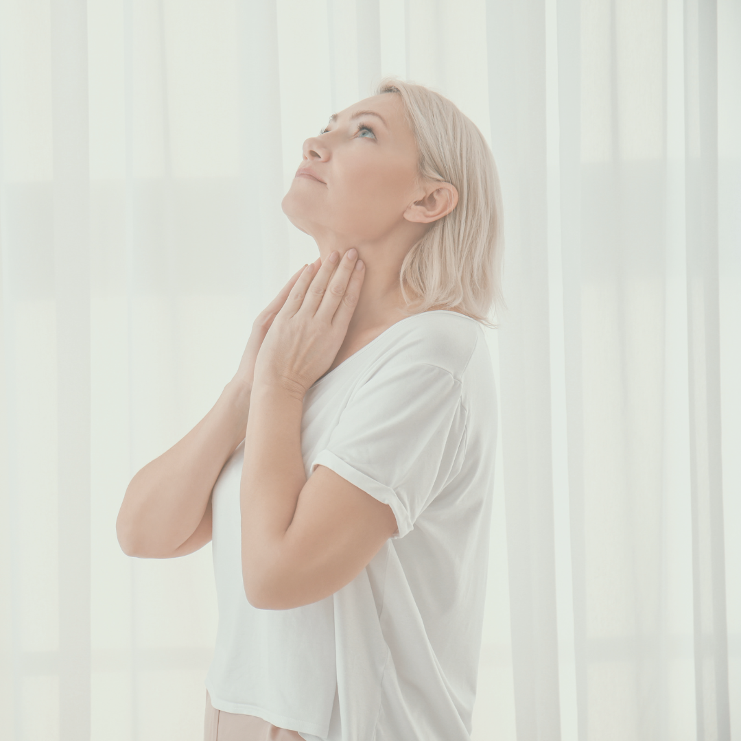 Blonde woman wearing a white shirt and holding her neck to show where her thyroid is.